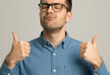 Portrait d’un homme sûr de lui, en chemise en jean et lunettes, affichant un petit sourire confiant avec les mains levées comme pour dire "je suis exceptionnel